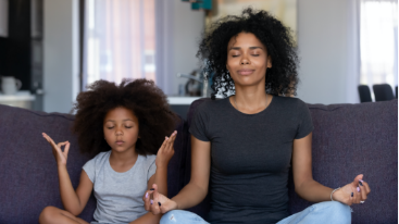 Image of a mom and her young daughter meditating on the couch.